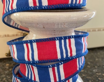 May include: Red, white, and blue striped ribbon spools. The ribbon is a woven fabric with a stitched edge.