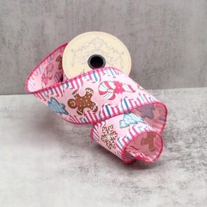 May include: A roll of pink Christmas ribbon with a festive pattern. The ribbon features gingerbread men, candy canes, snowflakes, and blue and white stripes. The ribbon is approximately 6.35 cm wide, ideal for holiday crafts and gift wrapping.