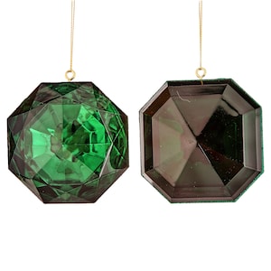 May include: Two green faceted glass ornaments shaped like large gemstones. Each ornament has a gold string attached for hanging.