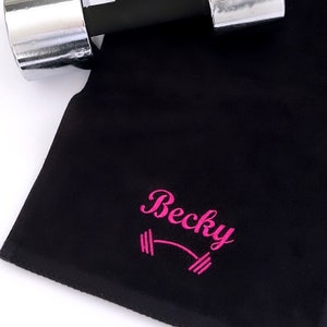 May include: Black microfiber fitness towel with pink embroidery. The embroidery says "Becky" with a barbell symbol.