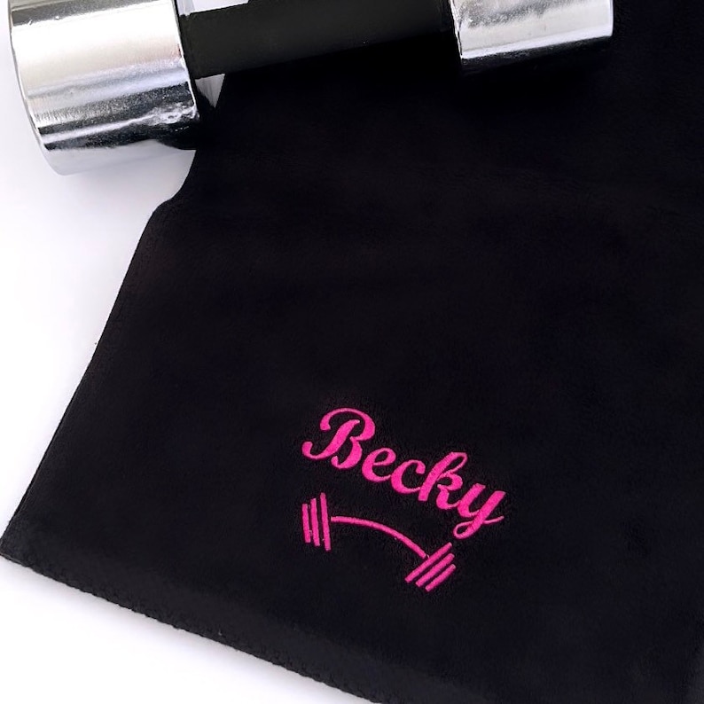 May include: Black microfiber fitness towel with pink embroidery. The embroidery says "Becky" with a barbell symbol.