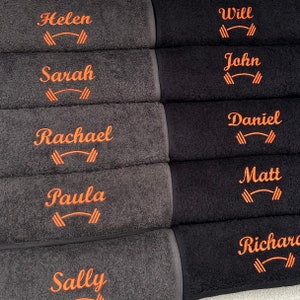 May include: Six black and gray towels with orange embroidered names and a dumbbell symbol. The names are Helen, Sarah, Rachael, Paula, Sally, Will, John, Daniel, Matt, and Richard.