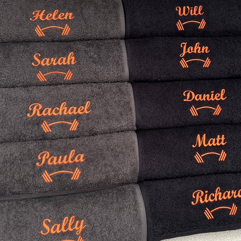May include: Six black and gray towels with orange embroidered names and a dumbbell symbol. The names are Helen, Sarah, Rachael, Paula, Sally, Will, John, Daniel, Matt, and Richard.