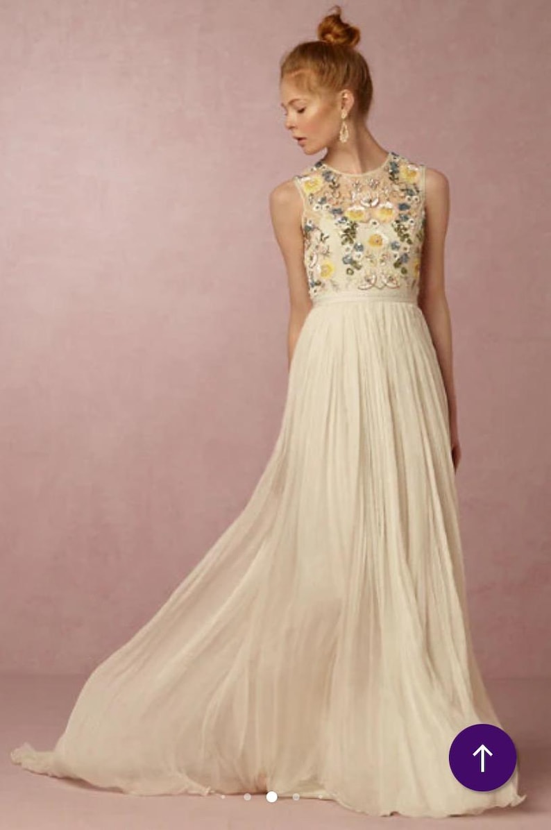 May include: A sleeveless ivory wedding dress with a floral embroidered bodice and a flowing pleated skirt. The dress features a high neckline and a long train. The floral embroidery includes yellow, blue, and green accents.