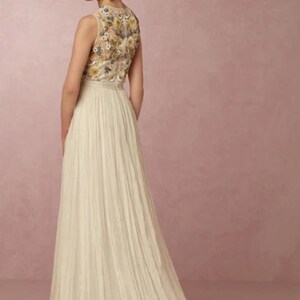 May include: A sleeveless ivory wedding dress with a floral embroidered bodice and a flowing pleated skirt. The dress features a long train and is suitable for bridal wear. The model has her hair up in a bun.