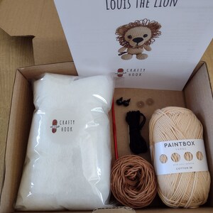 May include: A crochet kit for making a lion amigurumi toy. The kit includes beige and brown yarn, stuffing, safety eyes, a crochet hook, and instructions. The kit is packaged in a brown cardboard box with the words "Louis the Lion" and "Crafty Hook" printed on the lid.