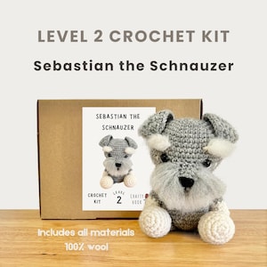 Op de afbeelding: Een haakpakket van niveau 2 met een grijze en witte Schnauzer-hond genaamd Sebastian. De kit bevat alle materialen en is gemaakt van 100% wol. De doos heeft de tekst "Level 2 Crochet Kit" en "Sebastian the Schnauzer."