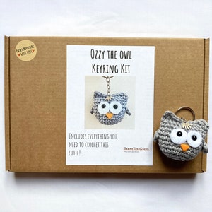 May include: A brown cardboard box with a white label that says "Ozzy the Owl Keyring Kit". The label also includes a picture of a gray crocheted owl with orange eyes and a yellow beak. The box includes everything you need to crochet this cute owl keyring.