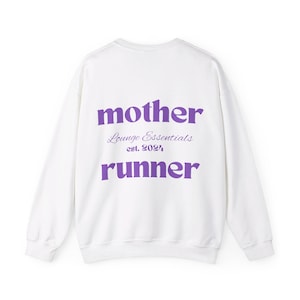 May include: White sweatshirt with the words "mother runner" in purple block letters. The words "Lounge Essentials est. 2024" are printed in a smaller, cursive font between the two words. The sweatshirt is a casual style.