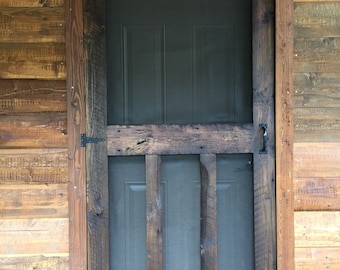 May include: A rustic wooden door with a screen door overlay. The door is painted a dark grey and has a simple design. The door is framed with a dark brown wood trim.