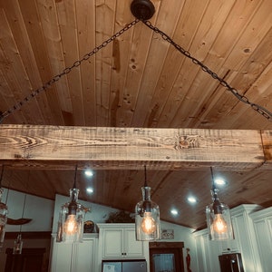May include: A rustic wooden beam chandelier with six clear glass bottle light fixtures and exposed Edison bulbs hanging from black chains. The chandelier is suspended from a wooden ceiling.