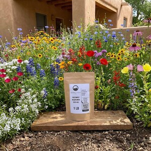Southwest wildflower garden blooming in front of an adobe-style home with a 1 lb seed mix bag displayed on a wooden board.