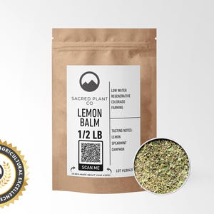 A resealable kraft paper bag labeled Sacred Plant Co Lemon Balm 1/2 LB with a close-up view of lemon balm leaves. The packaging emphasizes regenerative farming practices and includes tasting notes of lemon, spearmint, and camphor.
