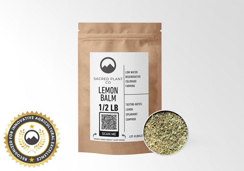 A resealable kraft paper bag labeled Sacred Plant Co Lemon Balm 1/2 LB with a close-up view of lemon balm leaves. The packaging emphasizes regenerative farming practices and includes tasting notes of lemon, spearmint, and camphor.