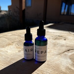 May include: Two blue glass bottles with dropper tops. The bottle on the left says "PAIR" and the bottle on the right says "REPAIR".