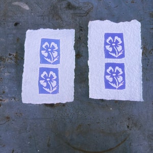 Puede incluir: Dos tarjetas de papel blanco con un dise&ntilde;o floral azul impreso en cada una. Las flores son estilizadas y tienen un dise&ntilde;o simple.
