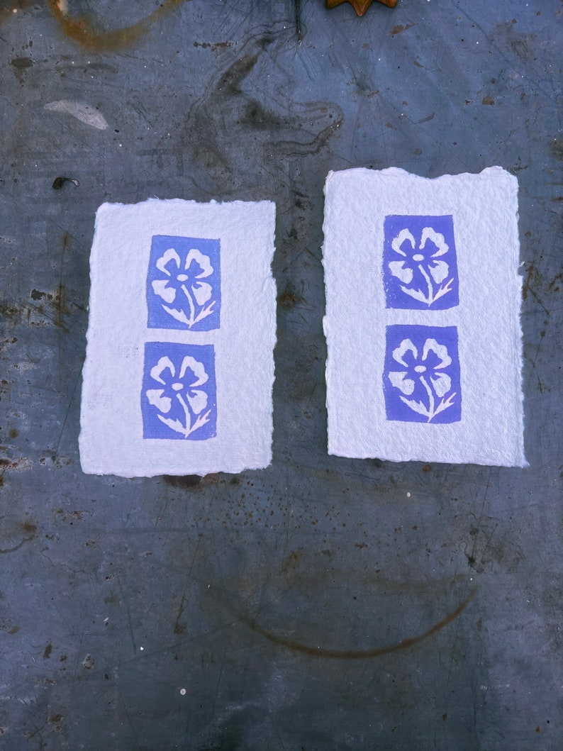 Puede incluir: Dos tarjetas de papel blanco con un dise&ntilde;o floral azul impreso en cada una. Las flores son estilizadas y tienen un dise&ntilde;o simple.