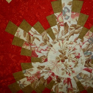 Könnte beinhalten: Nahaufnahme einer roten, weißen und braunen Steppdecke mit einem Blumenmuster. Die Steppdecke besteht aus verschiedenen Stoffen und ist in einem kreisförmigen Muster zusammengenäht.