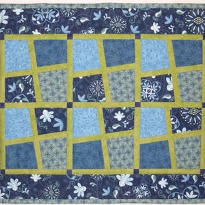 Könnte beinhalten: Eine blaue und grüne Steppdecke mit geometrischem Muster. Die Steppdecke besteht aus Quadraten und Rechtecken, und die Quadrate sind diagonal angeordnet. Die Steppdecke ist mit einem dunkelblauen Rand eingefasst.