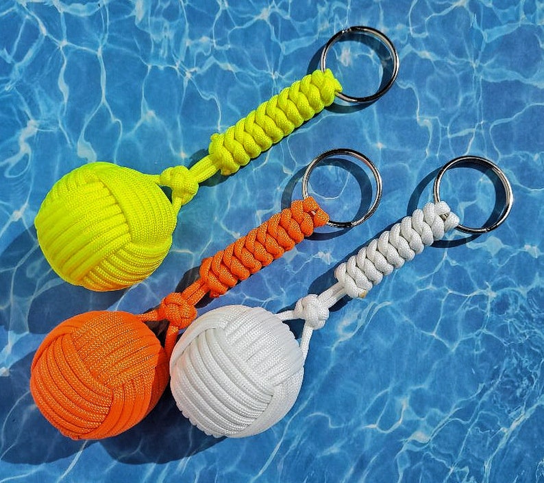 May include: Three keychains with colorful knotted balls attached to key rings. The balls are yellow, orange, and white.