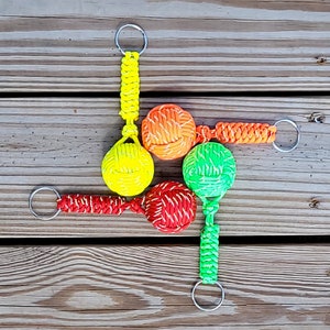 May include: Five colorful keychains with knotted balls attached to silver key rings. The balls are red, yellow, green, and orange.