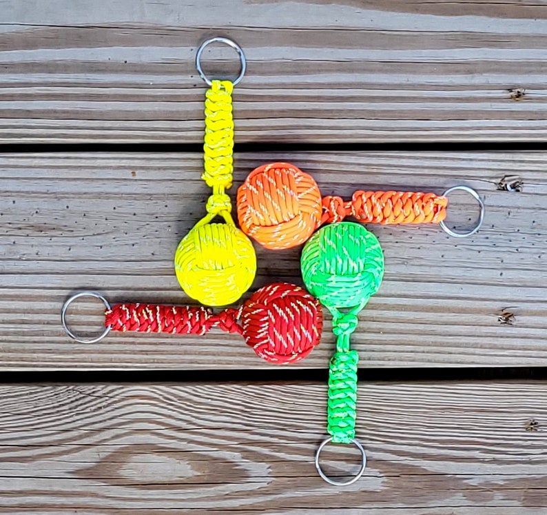 May include: Five colorful keychains with knotted balls attached to silver key rings. The balls are red, yellow, green, and orange.