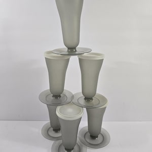 May include: A stack of six translucent gray plastic tumblers arranged in a pyramid formation. Each tumbler features a wide circular base, a tapered body, and a solid white circular lid that fits securely over the top rim of the vessel.