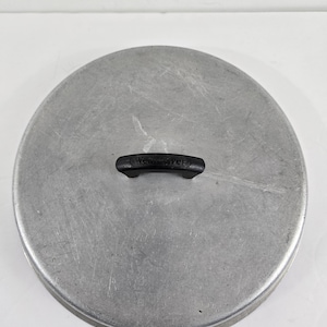 May include: A silver aluminum pot lid with a black plastic handle. The lid has a smooth surface with some scratches.