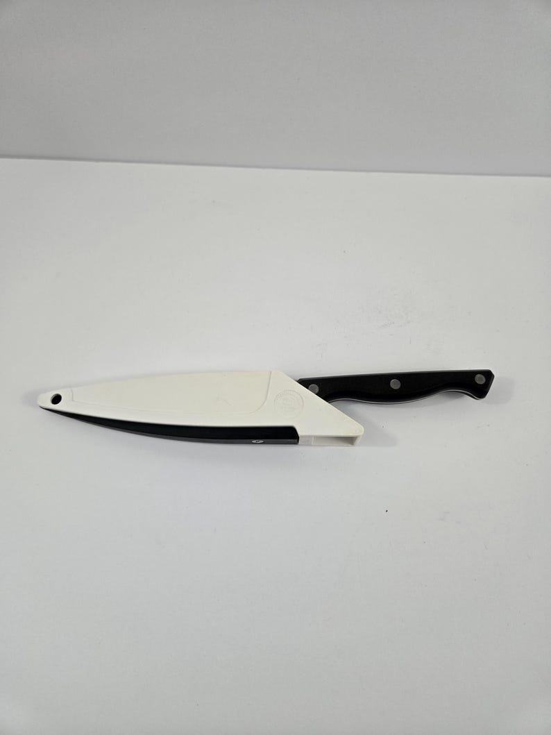 May include: A black and silver kitchen knife with a black handle and a white blade cover. The knife is designed for cutting and slicing food. The blade cover is white with a black trim.