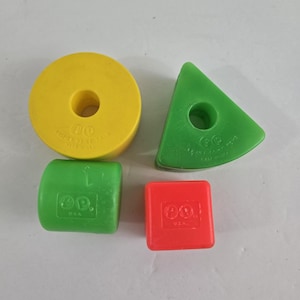 May include: A set of four colorful Fisher-Price toys. The shapes include a yellow ring, a green triangle, a green cylinder, and a red square. Each toy has a hole in the center and the text "Fisher-Price Toys" and "Made in USA".