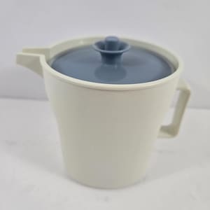 Può includere: Una caraffa in plastica color crema con manico e beccuccio abbinati. La caraffa è dotata di un coperchio circolare blu ardesia con un piccolo pomello centrale. Il corpo della caraffa ha una forma cilindrica leggermente affusolata.