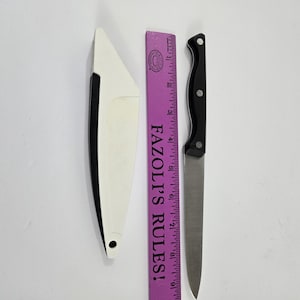 May include: A stainless steel knife with a black handle and a white knife sheath. A purple ruler with the text "FAZOLI'S RULES!" is next to the knife. The knife blade is approximately 20 cm long.