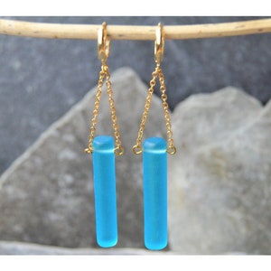 Könnte beinhalten: Ein Paar goldene Ohrringe mit einem hellblauen Glaszylinder-Anhänger an jedem Ohrring.