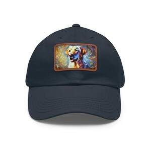 May include: Navy blue baseball cap featuring a colorful, artistic rendering of a golden Labrador Retriever. The artwork is set within a brown rectangular patch on the front of the cap. The cap has a curved brim and a classic six-panel design.
