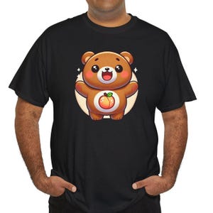 May include: Black t-shirt featuring a cartoon bear with a peach on its belly. The bear is brown with a white circle behind it and has a happy expression. The shirt is short-sleeved and has a crew neck.