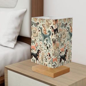 May include: A table lamp with a white fabric shade featuring a colorful pattern of dogs. The shade is decorated with a variety of dog breeds in different poses. The lamp has a wooden base.