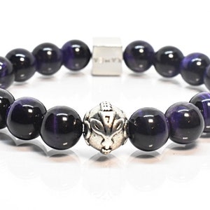 May include: A bracelet made of large, round, polished beads in deep purple and black. The bracelet features a silver-toned focal bead with an animal design. A small silver clasp is also visible.