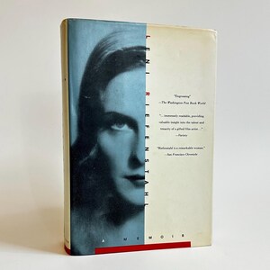 May include: A book cover featuring a woman's face on the front. The title of the book is "Leni Riefenstahl Memoir". The book cover is blue and white with red text.