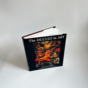 May include: A black hardcover book titled "The Occult in Art" by Owen S. Rachleff with an introduction by Isaac Bashevis Singer. The cover features a colorful illustration of a scene from a painting.