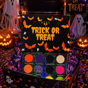Może przedstawiać: Czarna paleta do makijażu z napisem TRICK OR TREAT i grafikami pomarańczowych nietoperzy. Paleta zawiera osiem okrągłych cieni do powiek o nazwach Jack-o-Lantern, The Third Eye, Friday the 13th, You're My Boo, Caramel Apple, Burton, Creep oraz MONSTER.