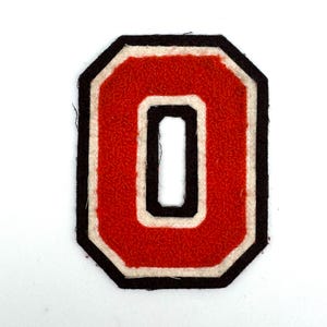 May include: A red felt letter "O" patch with a black and white border. The patch has a textured surface and a geometric shape. This patch is suitable for jackets, bags, or other apparel.