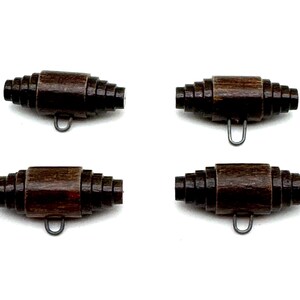 May include: Four dark brown wooden toggle buttons arranged in a grid. Each button features a cylindrical center with tiered, stepped ends that taper toward the tips. A small, thin metal loop is attached to the underside of each toggle button.