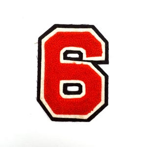 May include: A red, embroidered number six patch with a white border and a black outline. The number has a textured, fuzzy appearance and is set against a plain white background. This patch is suitable for apparel.