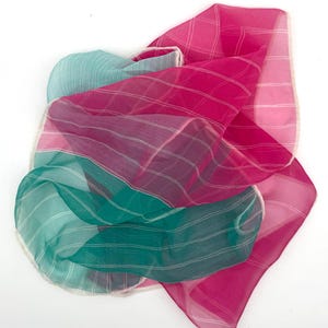 May include: A collection of sheer scarves in shades of teal, fuchsia, and pink. The scarves have a striped pattern with white lines and a delicate, white trim. The fabric appears lightweight and flowing, suitable for accessories.