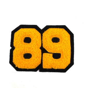 May include: A yellow felt patch with the number 89 in a varsity style. The numbers are outlined in black and have a textured appearance. The patch is likely for a jacket or other apparel.