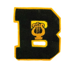 May include: A black felt letter B with a yellow outline. The letter has a gold lyre inside.