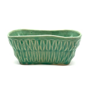 May include: A rectangular, light green ceramic planter with a textured, repeating diamond pattern. The planter has a slightly irregular rim and is set against a white background. The overall shape is a long rectangle.