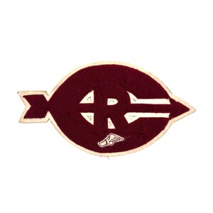 May include: A maroon and white patch with a stylized design. The patch features a maroon oval shape with a white border. Inside the oval is a white "R" with a small winged foot symbol.