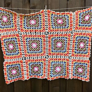 May include: A square crochet blanket featuring a repeating granny square pattern. The design consists of multiple colorful squares in shades of orange, red, yellow, blue, green, pink, and white, joined together with a white yarn border.