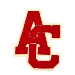 May include: A red and white felt patch featuring the letters "AC" in a bold, collegiate style. The letters are in a vibrant red color with a white border, set against a plain white background. The patch is likely for a jacket or bag.